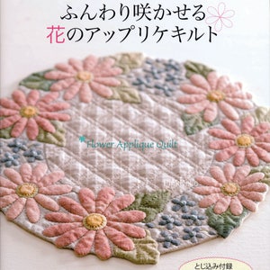 May include: A book cover featuring a flower applique quilt. The quilt is a circular design with pink daisy-like flowers, green leaves, and blue floral accents. The text reads "Flower Applique Quilt" and Japanese text.