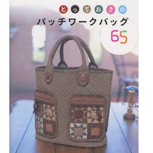 May include: A quilted tote bag with two front pockets, featuring patchwork designs in shades of brown, beige, and blue. The bag has a structured shape with two handles and decorative buttons. Japanese text is visible on the cover.