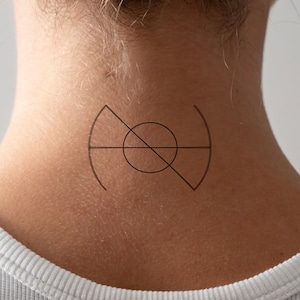 May include: A black temporary tattoo design on the neck. The design features a circle bisected by a diagonal line, with curved lines on either side. The tattoo is a minimalist geometric design.