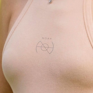 May include: A light peach-colored ribbed tank top with the word "NOAH" above a minimalist graphic. The graphic is a combination of geometric shapes, including a circle and triangles. The tank top is made of a soft, ribbed material.