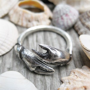 May include: A silver ring featuring a crab claw design. The ring is crafted from metal and has a smooth finish. The crab claws are detailed and lifelike.