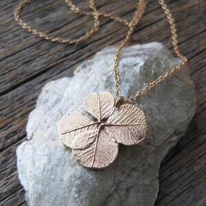 May include: A gold necklace featuring a four-leaf clover pendant. The pendant is crafted from metal and has an intricate design.