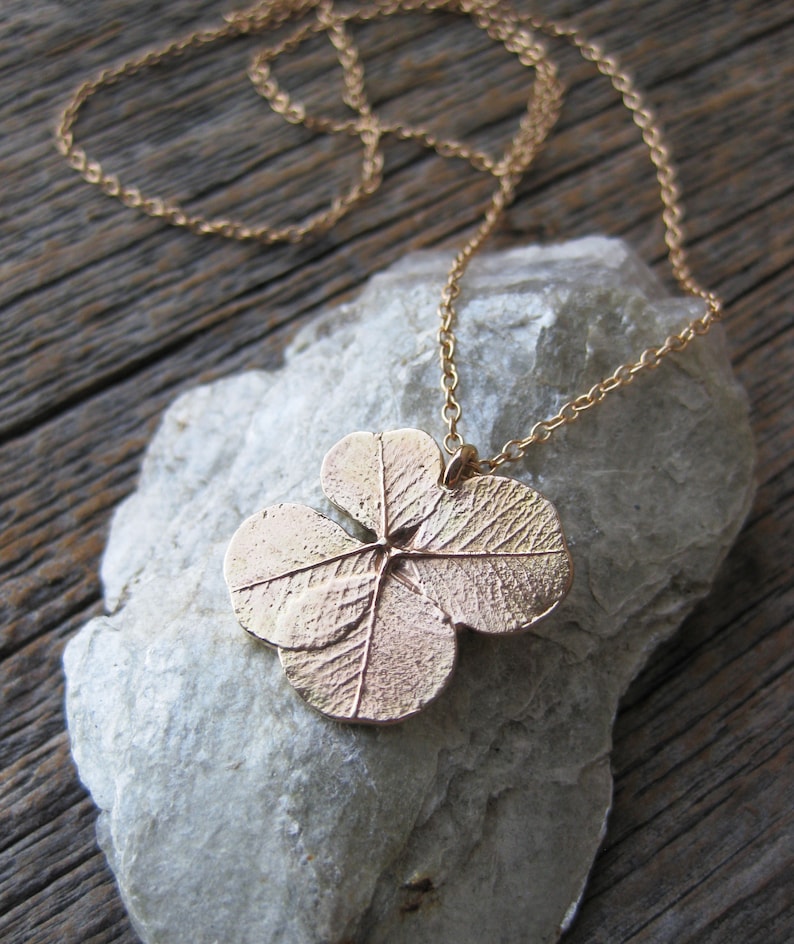 May include: A gold necklace featuring a four-leaf clover pendant. The pendant is crafted from metal and has an intricate design.