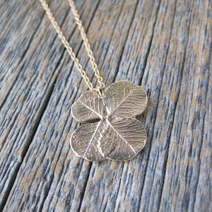May include: A gold necklace with a four-leaf clover pendant. The pendant is detailed with veins and a textured surface.