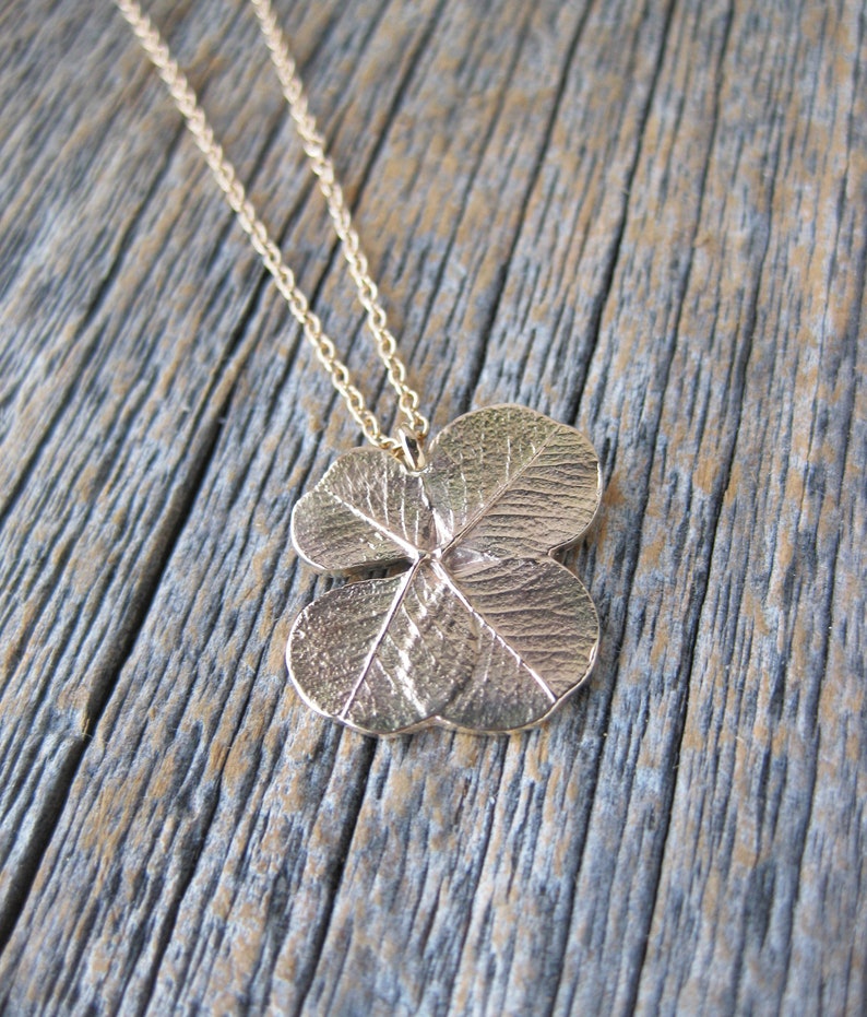 May include: A gold necklace with a four-leaf clover pendant. The pendant is detailed with veins and a textured surface.