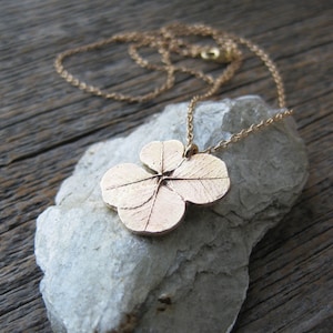 May include: A gold necklace featuring a four-leaf clover pendant. The pendant is detailed with veins and a textured surface.