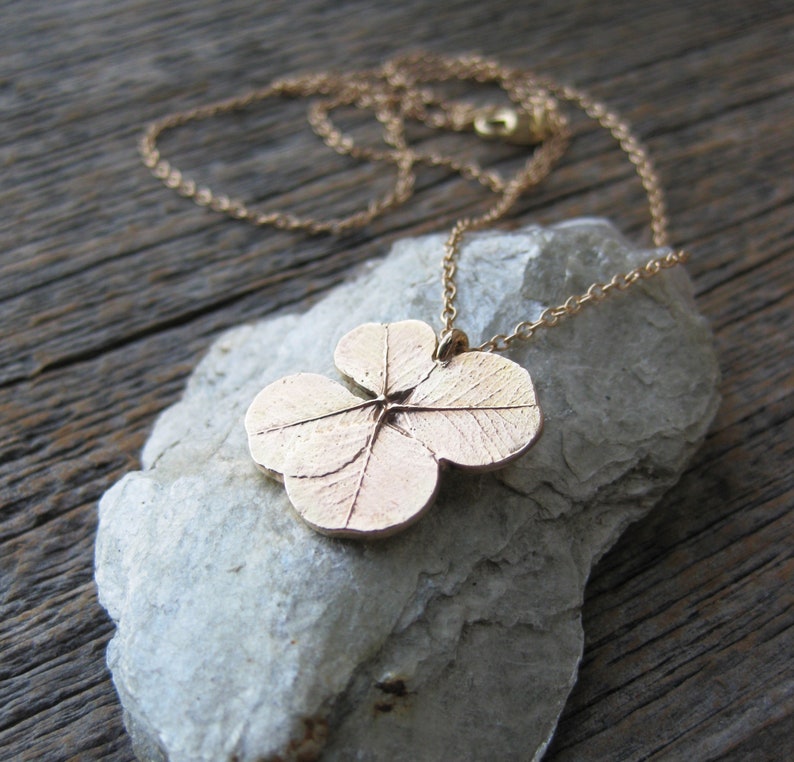 May include: A gold necklace featuring a four-leaf clover pendant. The pendant is detailed with veins and a textured surface.