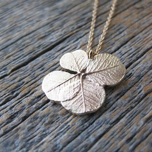May include: A gold four-leaf clover pendant necklace on a chain. The pendant is detailed with textured leaves.