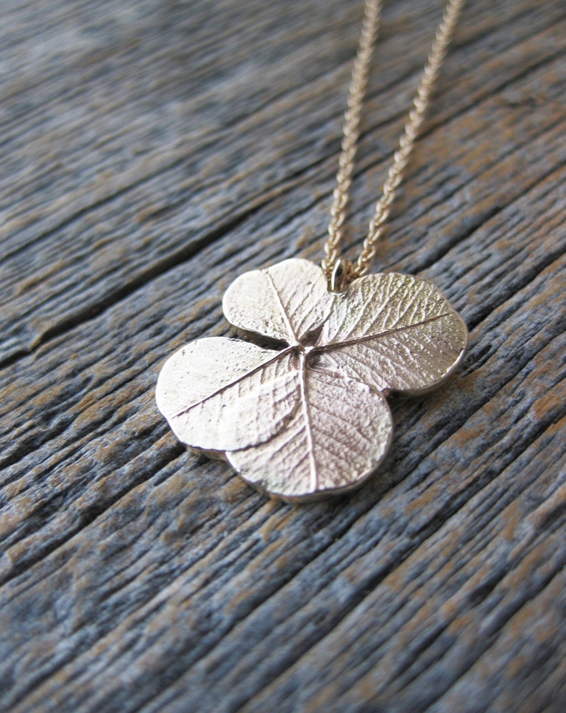 May include: A gold four-leaf clover pendant necklace on a chain. The pendant is detailed with textured leaves.