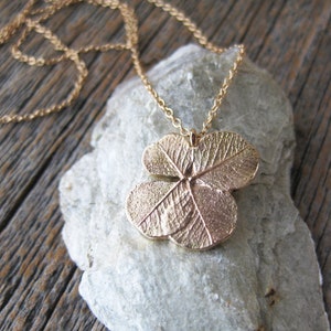 May include: A gold necklace featuring a four-leaf clover pendant. The pendant is detailed with veins and a textured surface.