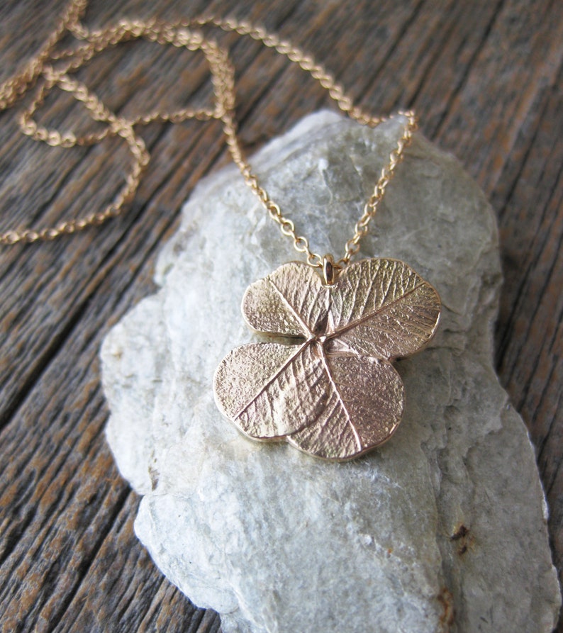 May include: A gold necklace featuring a four-leaf clover pendant. The pendant is detailed with veins and a textured surface.
