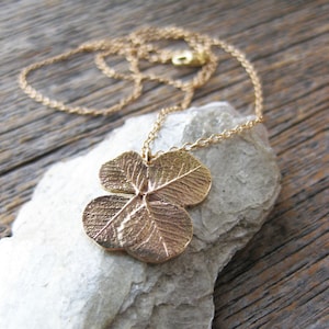 May include: A gold necklace featuring a four-leaf clover pendant. The pendant is crafted from metal and has a detailed design.