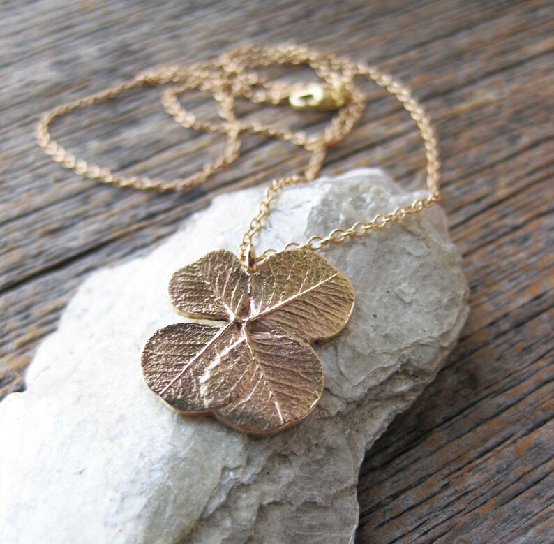 May include: A gold necklace featuring a four-leaf clover pendant. The pendant is crafted from metal and has a detailed design.
