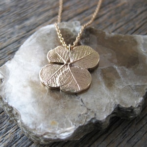 May include: A gold-toned necklace featuring a four-leaf clover pendant. The pendant is detailed with veins and a textured surface.