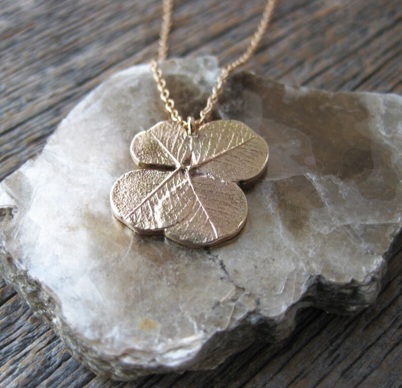 May include: A gold-toned necklace featuring a four-leaf clover pendant. The pendant is detailed with veins and a textured surface.