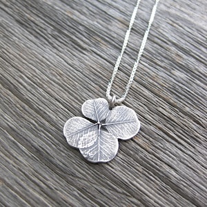 May include: A silver necklace with a four-leaf clover pendant. The pendant is detailed with a textured design.