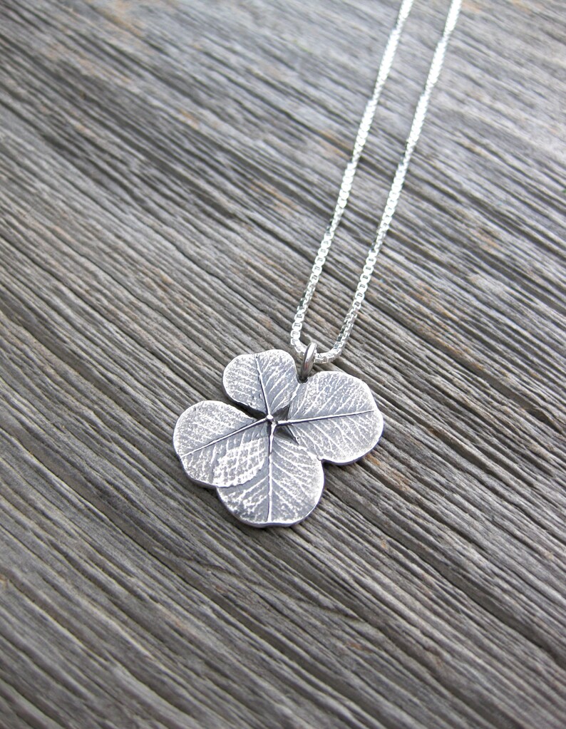 May include: A silver necklace with a four-leaf clover pendant. The pendant is detailed with a textured design.
