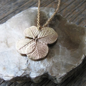 May include: A gold necklace featuring a four-leaf clover pendant. The pendant has a detailed textured leaf design.