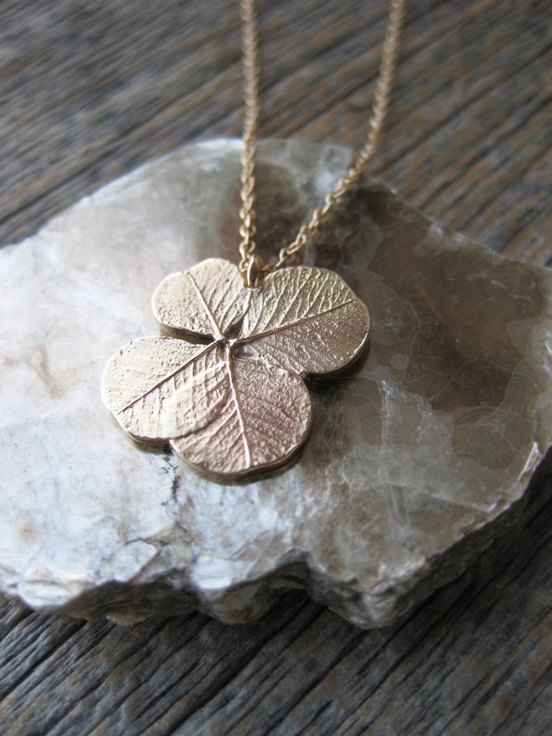 May include: A gold necklace featuring a four-leaf clover pendant. The pendant has a detailed textured leaf design.