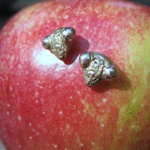 May include: Two silver-toned mouse-shaped earrings with small, round, white stones for eyes. The earrings are on a red apple.