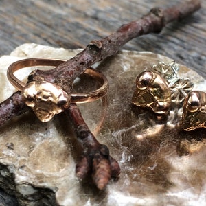 May include: A set of gold-toned jewellery featuring a ring and a pair of earrings. The ring has a textured, organic-shaped design. The earrings are stud earrings with a similar textured design.