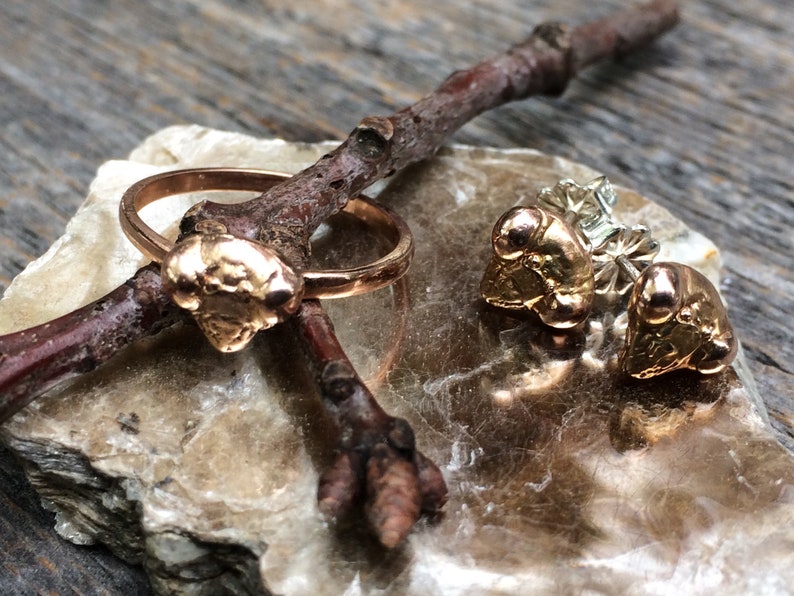 May include: A set of gold-toned jewellery featuring a ring and a pair of earrings. The ring has a textured, organic-shaped design. The earrings are stud earrings with a similar textured design.