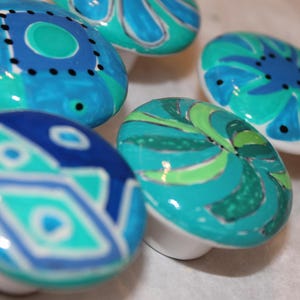 May include: Five ceramic knobs with a blue, green, and white swirl design. The knobs are round and have a glossy finish.