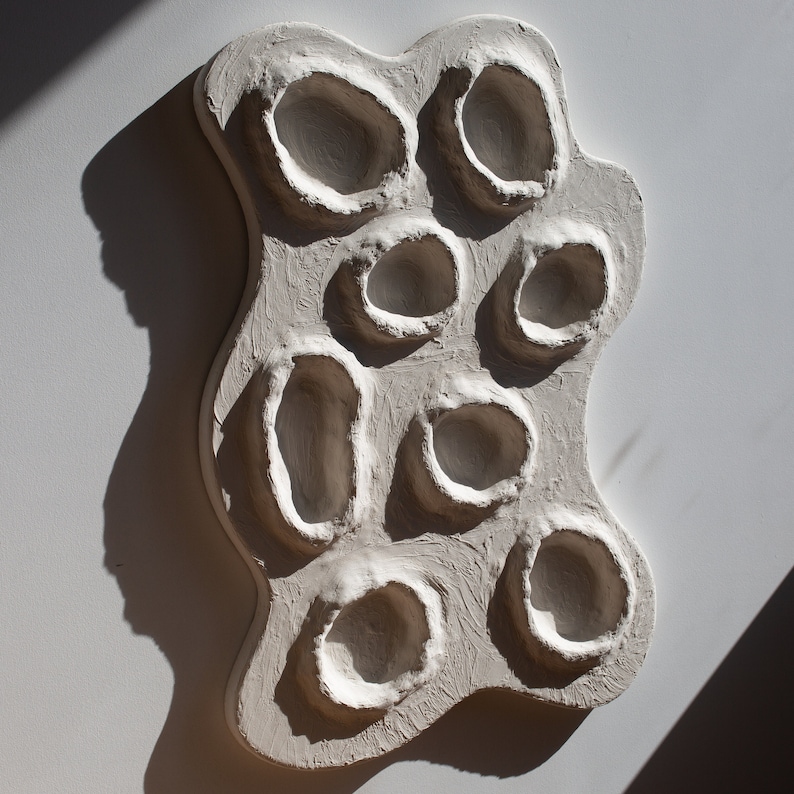 Pu&ograve; includere: Arte da parete in ceramica bianca con una superficie strutturata e pi&ugrave; rientranze circolari.