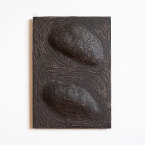 Pu&ograve; includere: Una scultura da parete in legno marrone scuro con due forme ovali in rilievo. La superficie della scultura ha un aspetto testurizzato e scolpito.