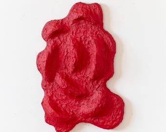 Könnte beinhalten: Eine rote abstrakte Skulptur mit einer strukturierten Oberfläche. Die Skulptur ist aus Papier gefertigt und hat eine einzigartige, organische Form.