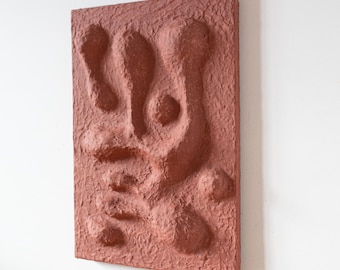 Può includere: Una scultura da parete color terracotta con un design astratto. La scultura è realizzata in carta testurizzata e ha una sensazione ruvida e organica.
