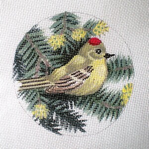 May include: A yellow bird with a red crown sits on a branch of green pine needles. The bird is surrounded by small yellow flowers.