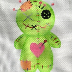 May include: A green voodoo doll with a pink heart, red stitches, and a black button eye. The doll has orange patches and is stitched together with red thread.