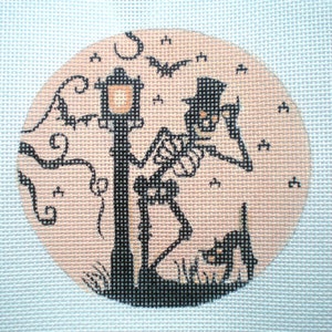 May include: A black and white embroidered design of a skeleton in a top hat standing next to a street lamp with a black cat in the foreground. The design is on a peach-colored background with bats flying in the air.