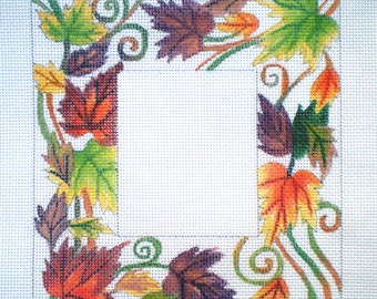 May include: A square frame with a white background and a border of colorful fall leaves. The leaves are in shades of red, orange, yellow, green, and brown. There are also some swirls in the border.