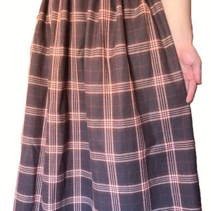 May include: A long, floor-length skirt featuring a dark brown base color with a prominent plaid pattern in light pink. The skirt has an elasticized waistband with gathered fabric, creating a full, flowing silhouette that extends to the hemline.