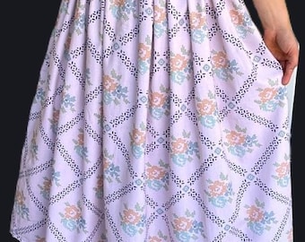 May include: A light purple skirt with an elastic waistband and a floral pattern. The skirt features a repeating design of flowers in peach and blue, set within a diamond grid of black dots.