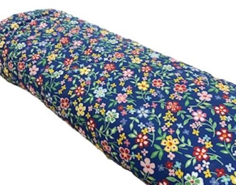 May include: A roll of fabric with a dark blue background and a colorful floral pattern. The flowers are in shades of red, yellow, pink, and white, with green leaves. The fabric is tightly rolled.