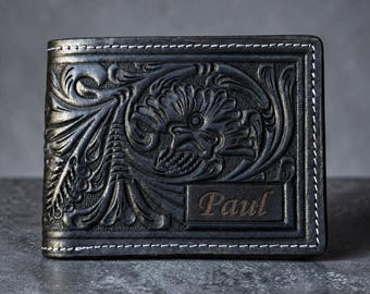 May include: Black leather wallet with an embossed floral design and the name "Paul" on a rectangular plaque. The wallet has white stitching around the edges.
