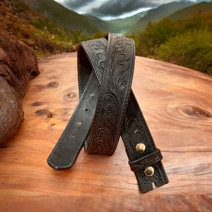 May include: A black leather belt with an intricate floral design. The belt has a buckle with gold accents.