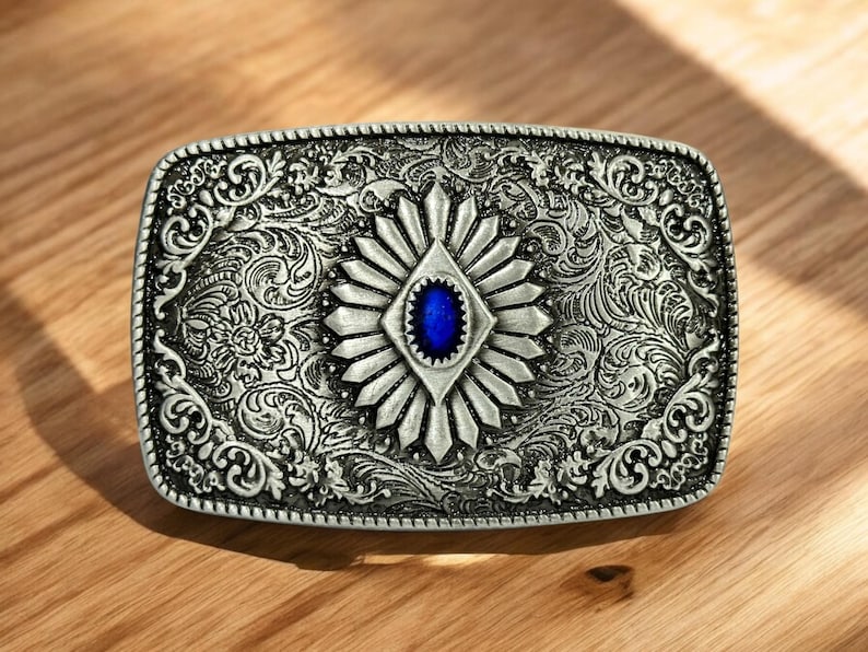 May include: Silver belt buckle with an ornate design featuring a blue gemstone in the center.
