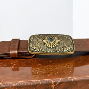 May include: A brown leather belt with a gold-toned buckle featuring an ornate design and a blue gemstone in the center.