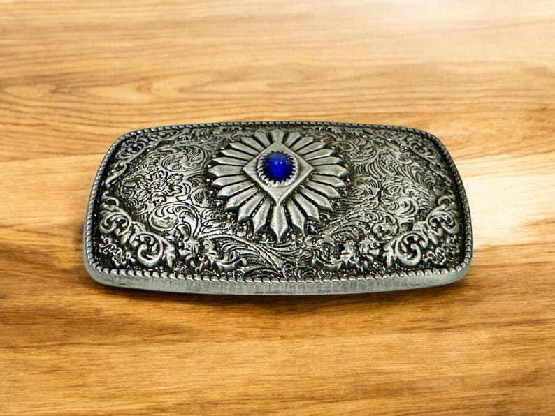 May include: Silver belt buckle with an ornate design and a blue gemstone in the center.