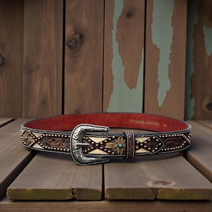 May include: A brown leather belt with a silver buckle and decorative floral and geometric patterns. The belt has turquoise accents and is 34 inches long.