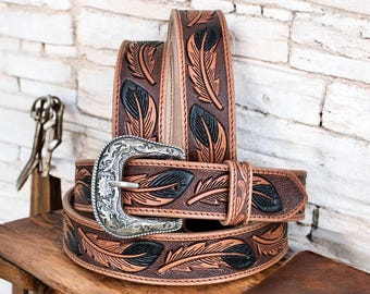 May include: A brown leather belt featuring a repeating embossed feather pattern with black accents. The belt includes a silver-toned metal buckle with intricate floral engravings and a matching leather keeper loop to secure the strap in place.