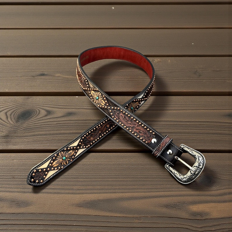 May include: A brown leather belt with intricate floral and leaf patterns, accented with small gold-colored studs and turquoise-colored stones. The belt has a silver-colored buckle and a red interior lining.
