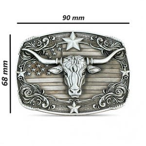 May include: Silver-toned metal belt buckle featuring a longhorn steer head with large horns, set against a backdrop of the American flag. The buckle measures 3.5 inches wide and 2.7 inches high.