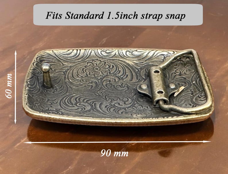 May include: A gold-toned belt buckle with an ornate floral design. It measures 3.5 inches by 1.5 inches and is labeled "Fits Standard 1.5 inch strap snap".
