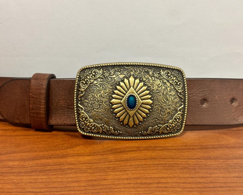 May include: A brown leather belt with a gold-toned buckle featuring an ornate design and a blue gemstone in the center.