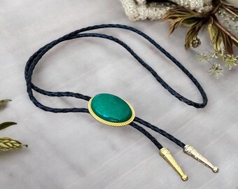 May include: A green oval gemstone bolo tie with a gold setting and black braided cord.